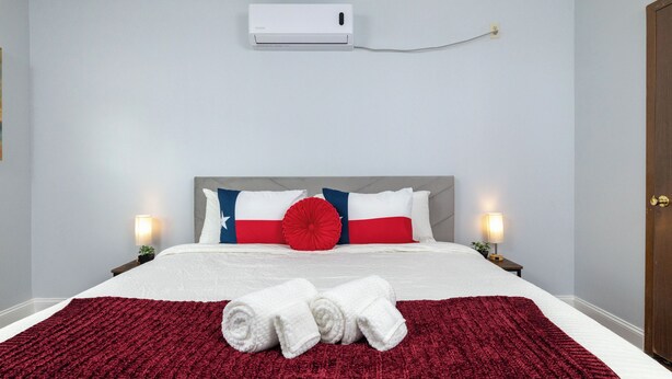 Una habitación de hotel con cama, almohadas, una colcha y un equipo de aire acondicionado.