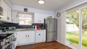 Una cocina moderna con armarios blancos, un refrigerador de acero inoxidable, un horno empotrado y una ventana con vistas al exterior.