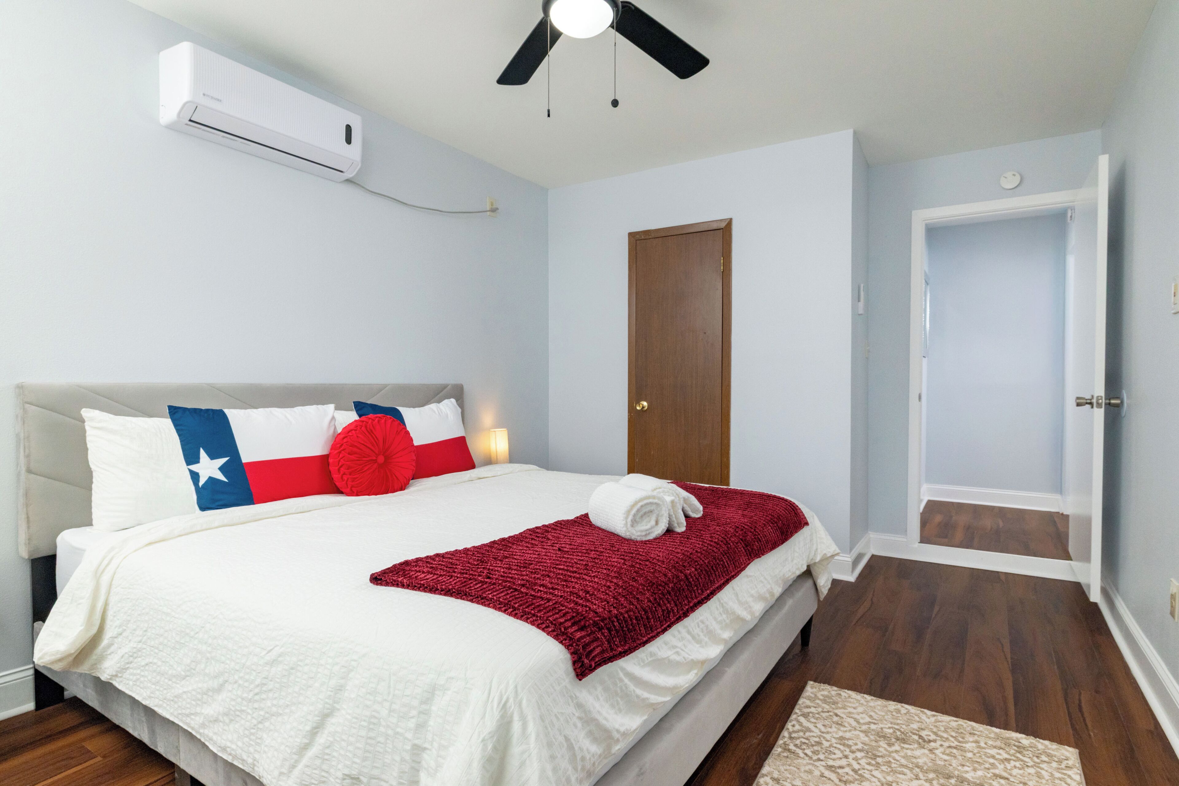 Une chambre à coucher comprenant un lit, un ventilateur de plafond, un appareil de climatisation, une porte en bois et un couloir.