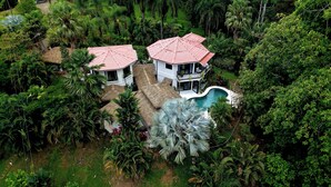 Duas casas com telhados vermelhos, cercadas por vegetação exuberante e uma piscina.