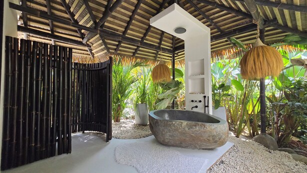Um espaço ao ar livre coberto com uma banheira de pedra, paredes de bambu e vegetação exuberante.
