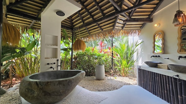 Un baño con un lavabo de piedra grande, un lavamanos blanco y un espejo.