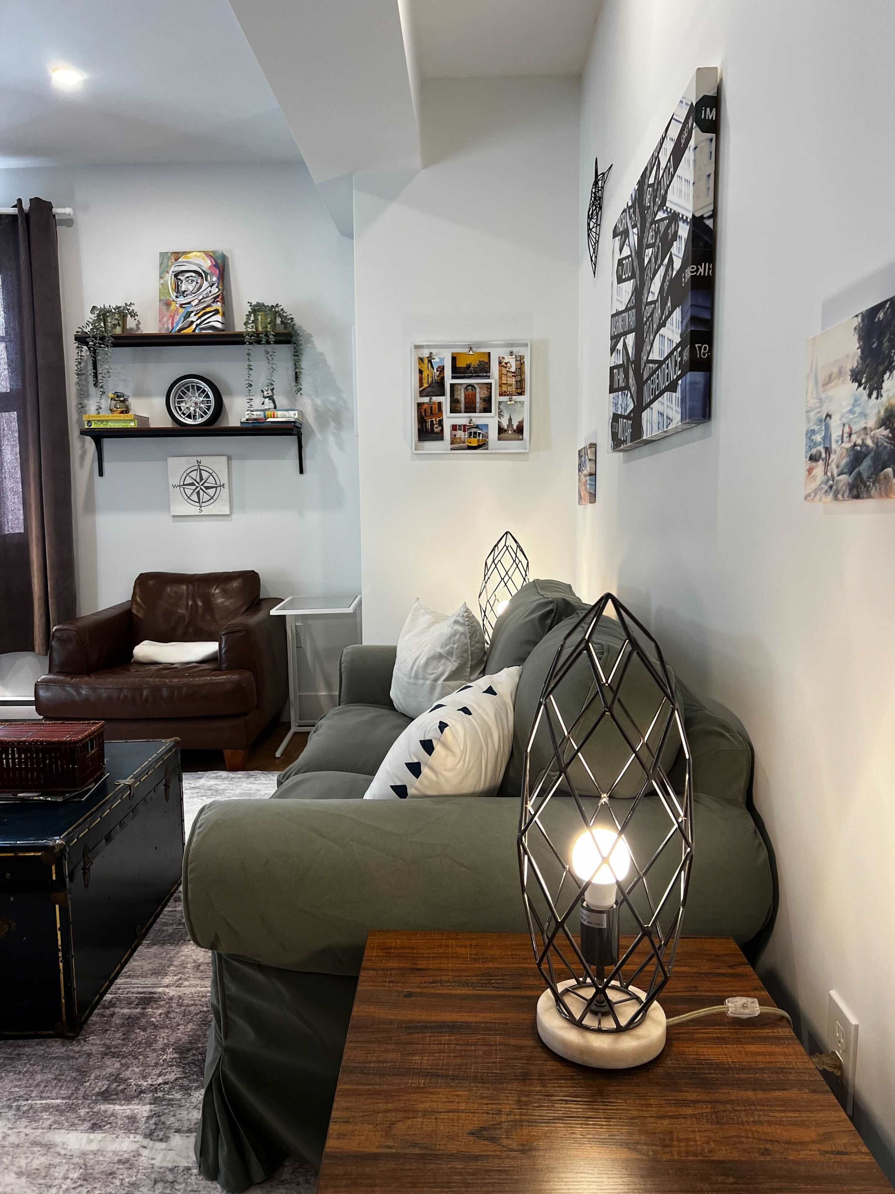 A modern living room with a green sofa, a leather armchair, a wooden coffee table, and a decorative lamp.