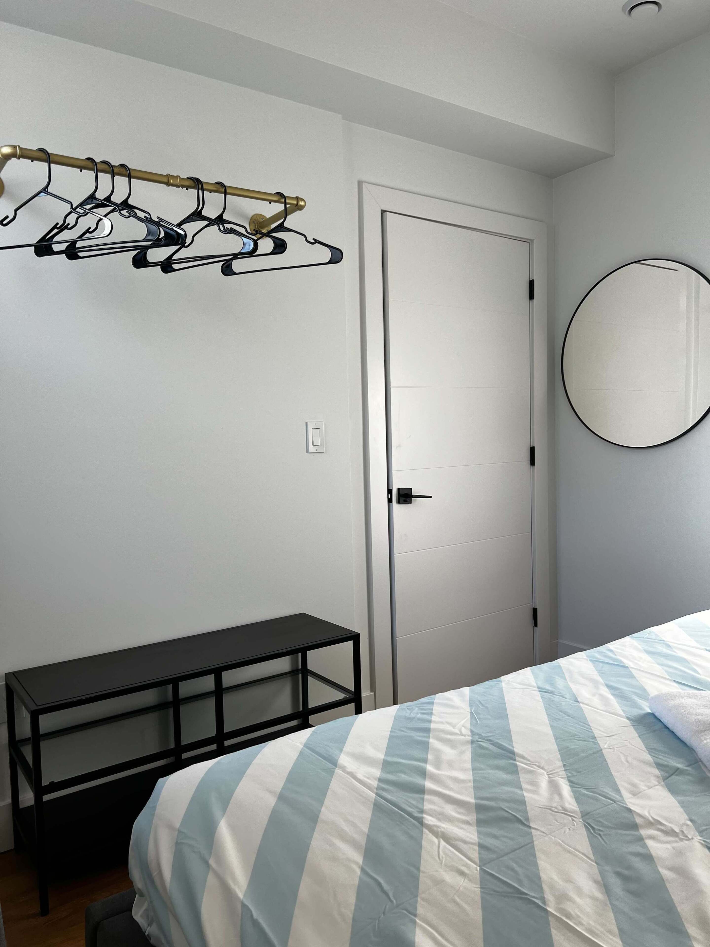 Een slaapkamer met een bed, een bankje, een deur en een spiegel aan de muur.