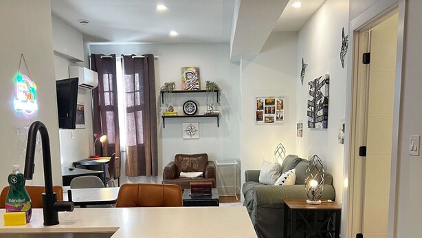Una cucina moderna con lavastoviglie in acciaio inossidabile, un'area pranzo con tavolo e sedie, un soggiorno con divano e tavolino e un corridoio con una porta.