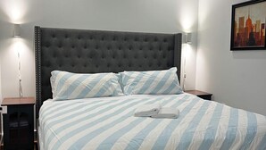 Un letto rifatto con cura, con lenzuola a righe, una testiera imbottita e due lampade ai comodini.