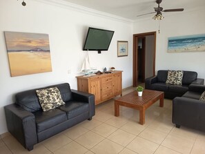 A living room with a sofa, coffee table, TV, and artwork on the walls. - Villa Heartly – Luxury, Tranquillity & Panoramic Sea Views (Playa Blanca)