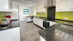 A modern kitchen with white cabinets, a black countertop, and a green backsplash. - Villa Heartly – Luxury, Tranquillity & Panoramic Sea Views (Playa Blanca)