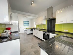 A modern kitchen with white cabinets, a black countertop, and a green backsplash. - Villa Heartly – Luxury, Tranquillity & Panoramic Sea Views (Playa Blanca)