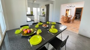 A modern kitchen with a dining table set for six, equipped with a refrigerator, oven, and ample counter space. - Villa Heartly – Luxury, Tranquillity & Panoramic Sea Views (Playa Blanca)