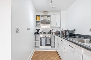A modern kitchen with white cabinets, a stainless steel range hood, and a black countertop. - 1-bedroom Apartment in Birmingham (Birmingham)