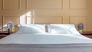 Ein ordentlich bezogenes Bett mit weißen Leinen, einem Dekokissen und zwei Nachttischlampen auf Holz-Nachttischen.