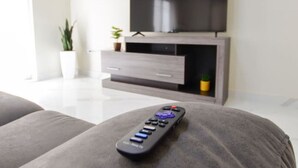 A modern living room with a flat-screen TV, a remote control, and a grey sofa.