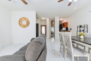 Ein modernes Wohnzimmer mit grauem Sofa, einem Esstisch mit Stühlen, einer Küchenzeile und einer Wanddekoration.