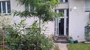 A stone pathway leading to a building with a wooden table and potted plants in the foreground. - „Modern apartment 5 min from metro Anděl – fast WiFi“ (Praha)