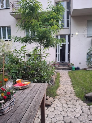 A stone pathway leading to a building with a wooden table and potted plants in the foreground. - „Modern apartment 5 min from metro Anděl – fast WiFi“ (Praha)