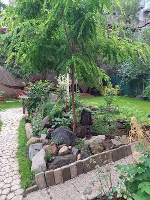 A garden with a stone pathway, a hammock, and various plants. - „Modern apartment 5 min from metro Anděl – fast WiFi“ (Praha)