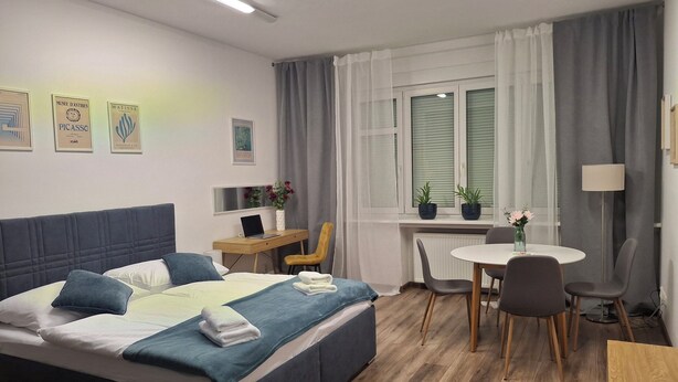 A hotel room with a bed, desk, chair, dining table, and potted plants. - „Modern apartment 5 min from metro Anděl – fast WiFi“ (Praha)