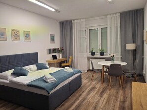 Een hotelkamer met een bed, bureau, stoel, eettafel en potplanten.
