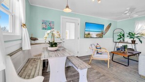 Une pièce avec un banc en bois, une table sur laquelle est posée une plante, une chaise, un ventilateur de plafond et un tableau accroché au mur.