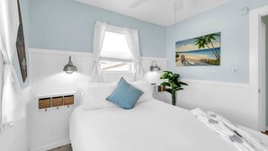 Une chambre à coucher avec un lit, une fenêtre avec des rideaux, une lampe fixée au mur, une plante et un tableau.