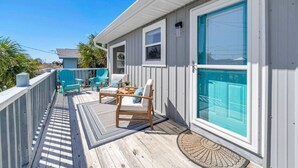 Une terrasse en bois avec des meubles d’extérieur, une porte dotée d’une fenêtre et un petit espace de véranda.