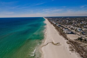 Luchtbeeld van een kustgebied met een strand, een weg en woongebouwen.