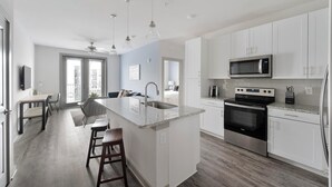 Una cocina moderna con armarios blancos, una isla central, electrodomésticos de acero inoxidable y un comedor con vistas.