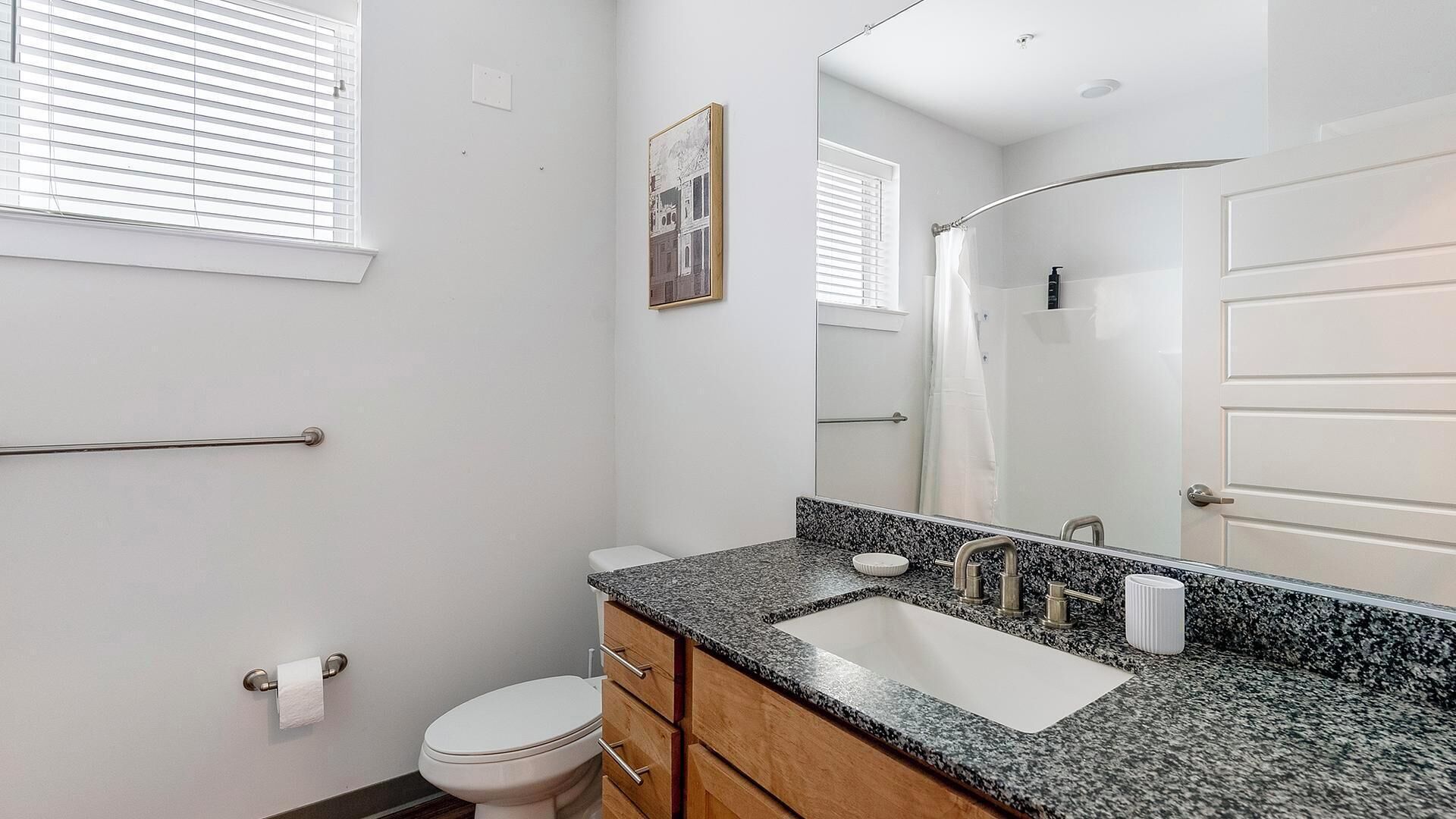 A bathroom with a white toilet, a granite countertop sink, a large mirror, and a towel rack.