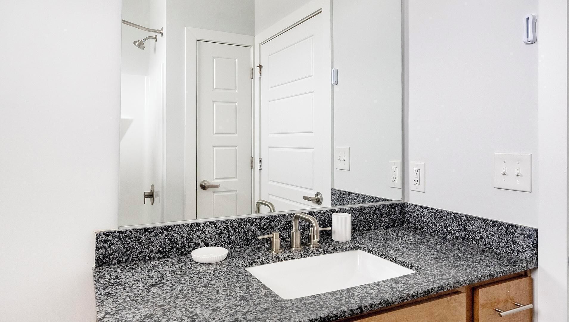 Een badkamer met een granieten aanrecht, een wit wastafel, een spiegel en een douche.