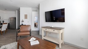 Ein modernes Wohnzimmer mit Couchtisch aus Holz, Ledersessel, Schreibtisch mit Flachbildfernseher und einer Küche im Hintergrund.