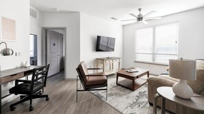 Ein moderner, gut beleuchteter Raum mit Schreibtisch, Bürostuhl, Sofa und Deckenventilator.