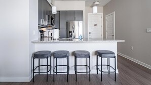 Cozinha moderna com armários cinza, eletrodomésticos de aço inoxidável, bancada de mármore e quatro banquetas.