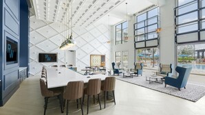 Um lobby de hotel moderno com um grande balcão de recepção branco, assentos confortáveis e janelas amplas com vista para a área da piscina externa.