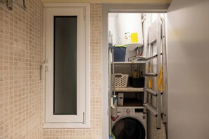 Ein Waschraum mit Waschmaschine, Regalen für Waschmittel und einem Fenster.