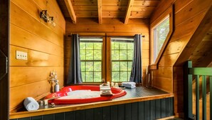 Una baita di legno con vasca idromassaggio, ampie finestre e vista sul verde.