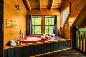 A wooden cabin with a hot tub, large windows, and a view of greenery. - 5* IndoorPool~Fireplace~FireTbl~Hot Tub~PS5~Bears (Gatlinburg)