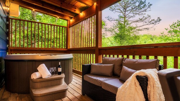 Un terrazzo in legno con vasca idromassaggio, divano in vimini e vista sul verde.