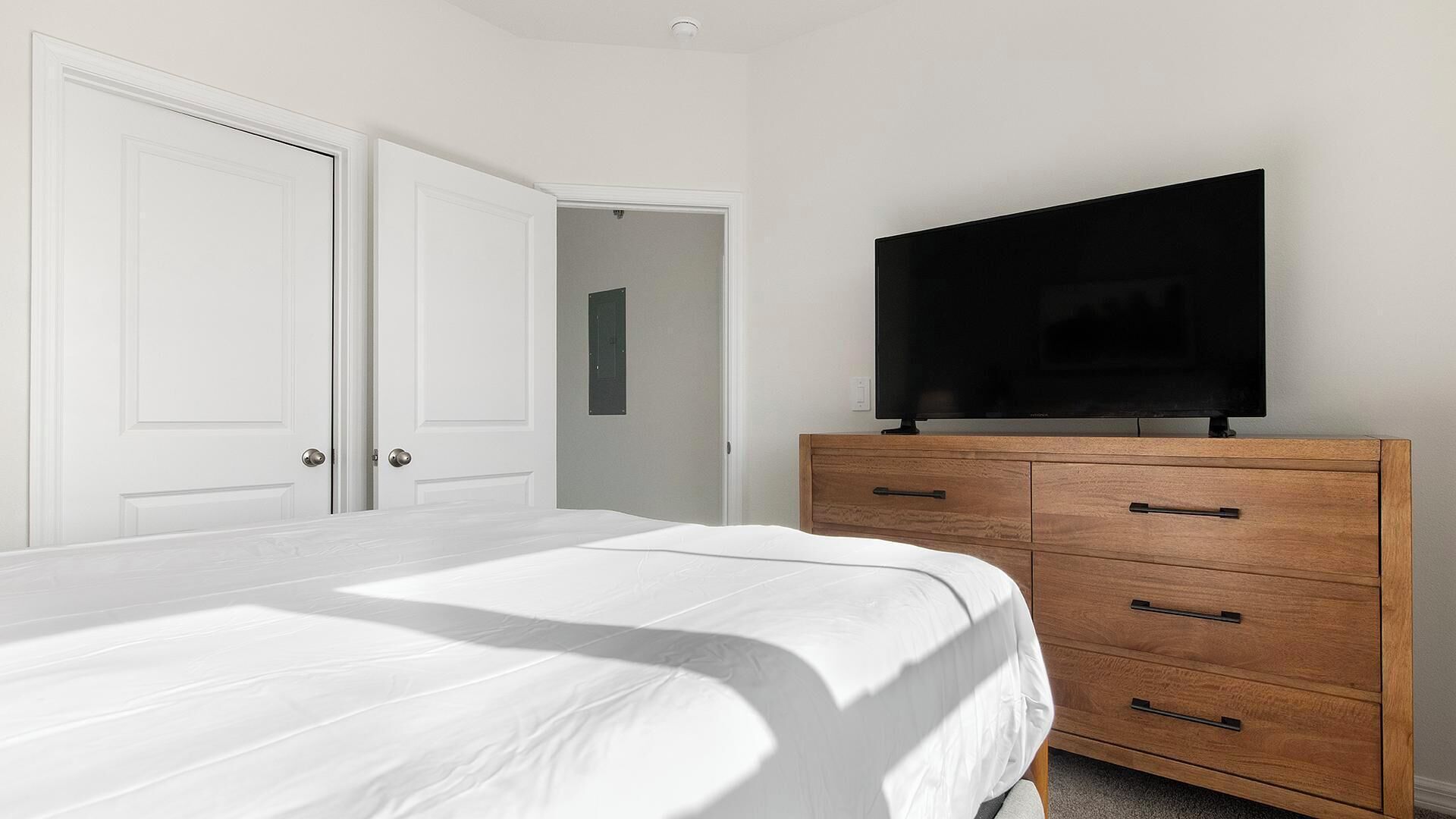 Ein Schlafzimmer mit einem Bett, einem Holzschrank, einem Fernseher und zwei weißen Türen.