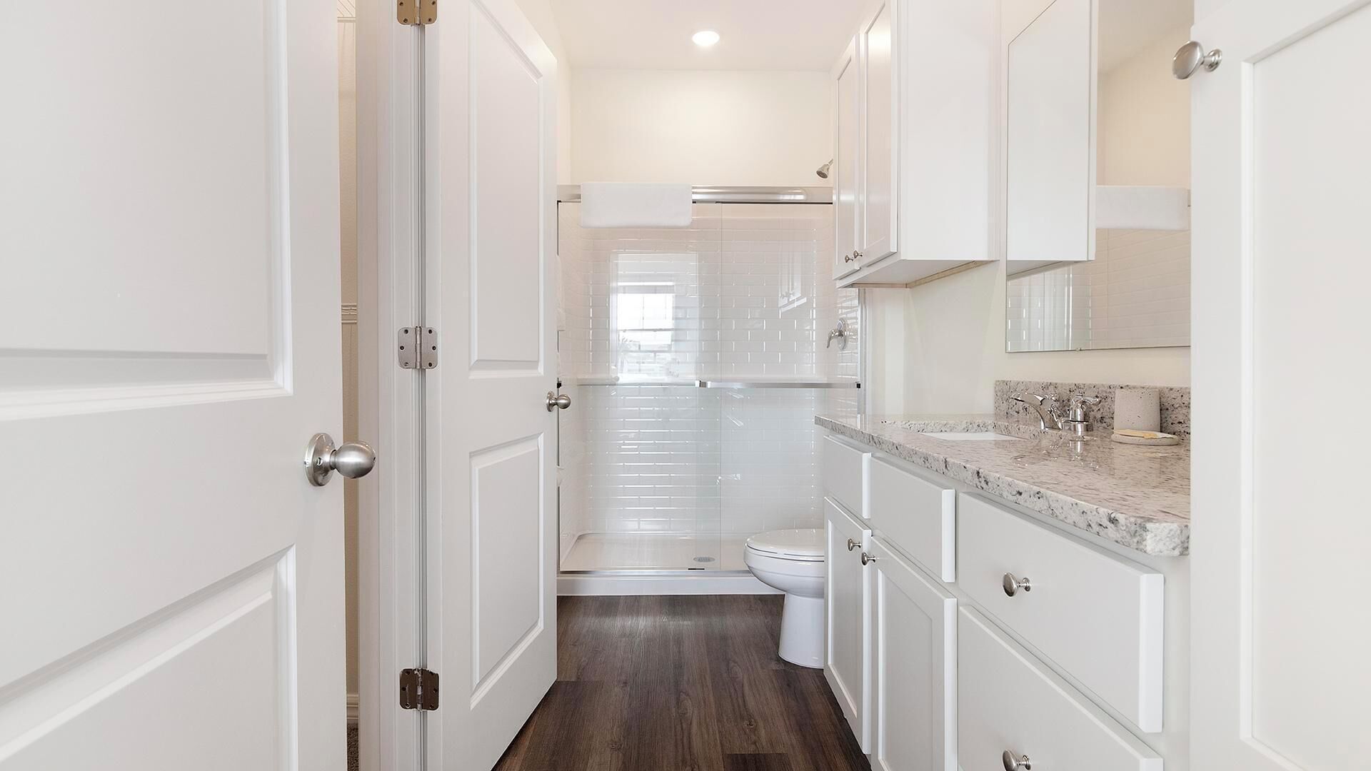 A narrow hallway leading to a bathroom with a toilet, sink, and mirror.