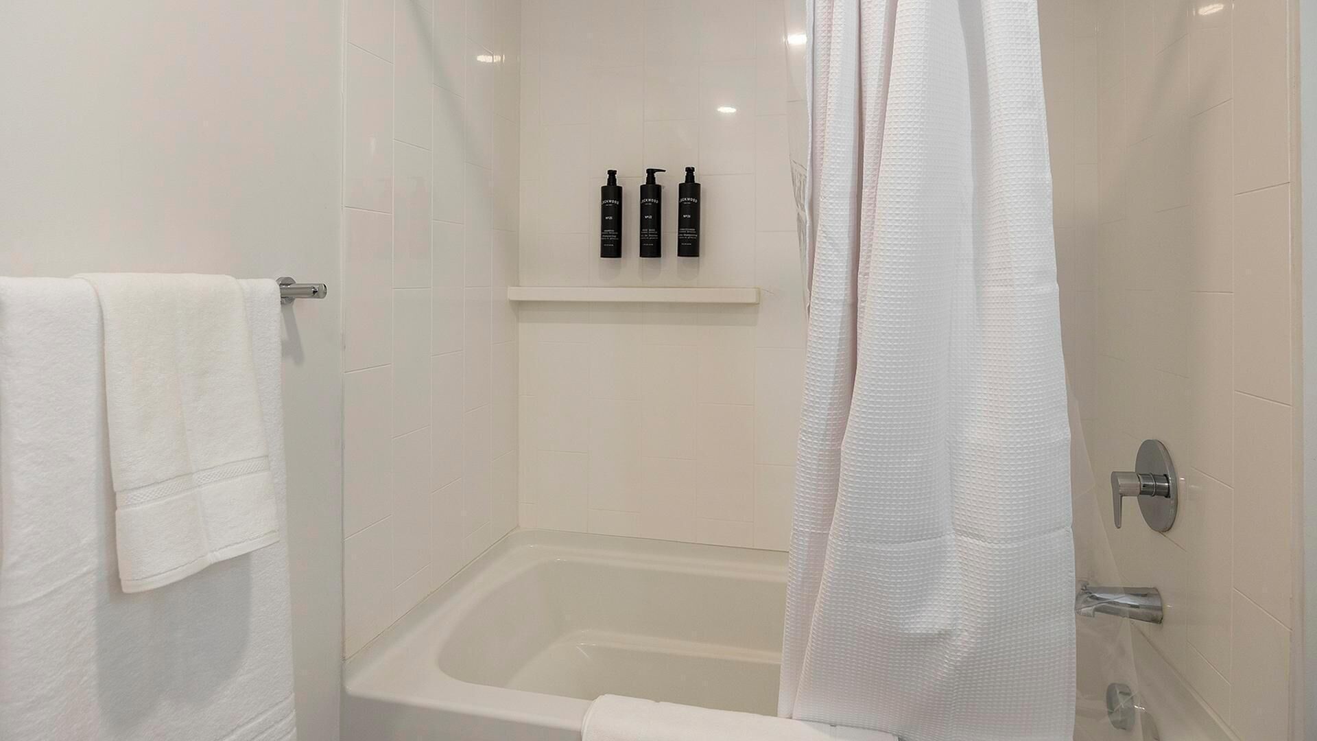 A modern bathroom with a white bathtub, a shower curtain, and a shelf with toiletries.