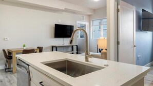 Eine moderne Küche mit einer großen Spüle, einem Essbereich mit Tisch und Stühlen, einem an der Wand befestigten Flachbildfernseher und einem Fenster mit Jalousien.