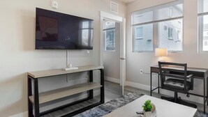 Ein modernes Wohnzimmer mit einem Flachbildfernseher, einem kleinen Tisch mit Lampe, einem Sessel und einer Konsole mit TV-Stand.