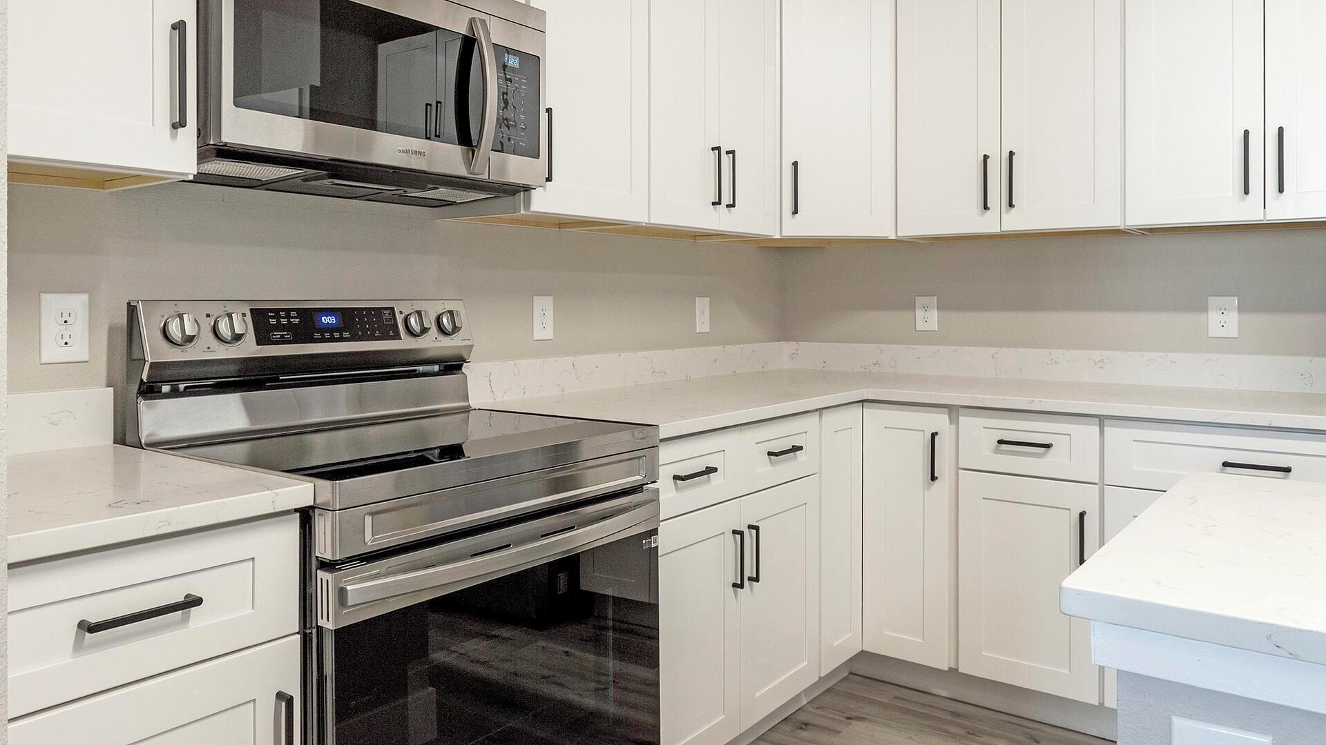A modern kitchen with stainless steel appliances, white cabinetry, and a marble countertop.