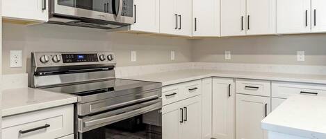 A modern kitchen with stainless steel appliances, white cabinetry, and a marble countertop.