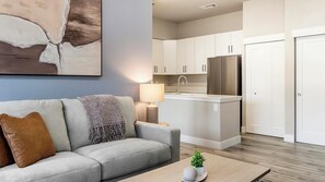 Una sala de estar moderna con un sofá, una mesa de centro, una lámpara y una zona de cocina con armarios y un refrigerador.