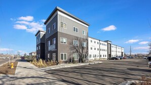 A multi-story building with a mix of dark and light facades, a parking lot, and a clear sky. - Landing | Amazing 2BD in Harvey Park South (Englewood)