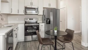 A modern kitchen with stainless steel appliances, a built-in oven, a microwave, and a refrigerator. There is a dining area with two chairs and a small table. - Landing | Amazing 2BD in Harvey Park South (Englewood)