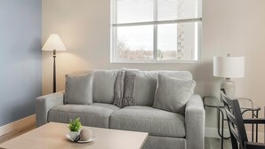 A living room with a sofa, a coffee table, a lamp, and a window with blinds. - Landing | Amazing 2BD in Harvey Park South (Englewood)