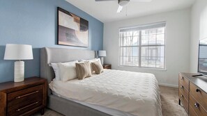 A bedroom with a bed, nightstands, a dresser, a ceiling fan, a window, and a painting on the wall. - Landing | Beautiful 1BD, Clubhouse (Jacksonville)